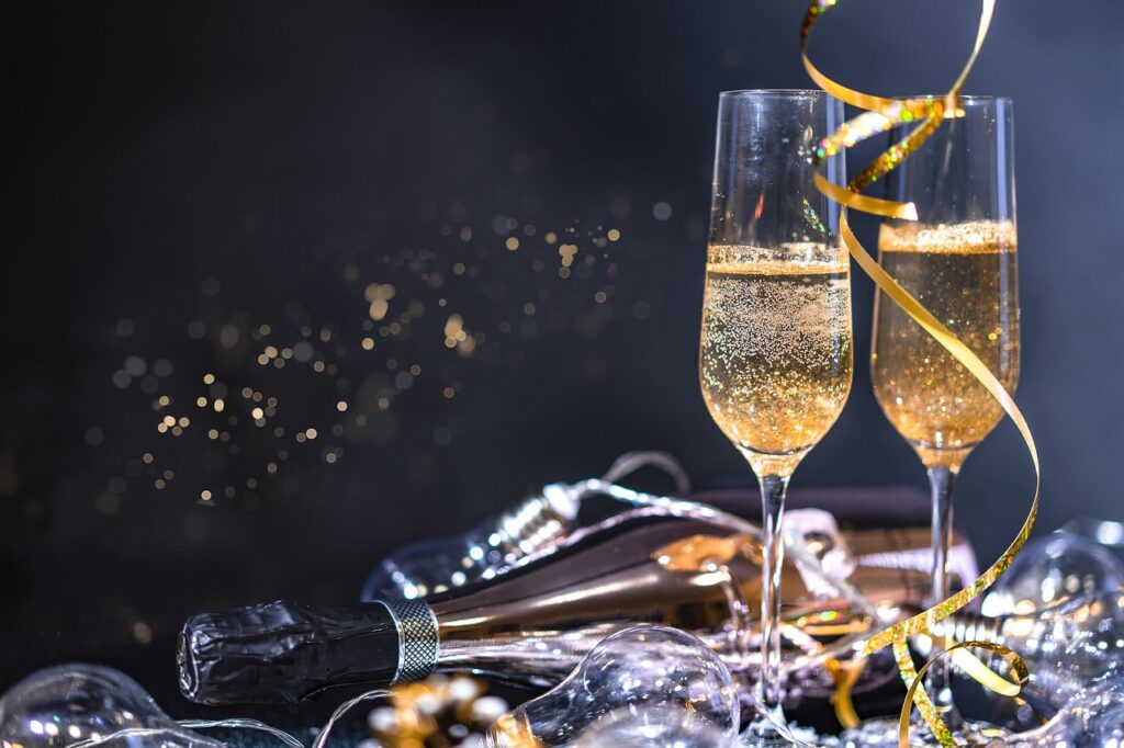 Två glas med bubblande champagne, en champagneflaska och guldfärgat festligt band – en stilfull firande stund.